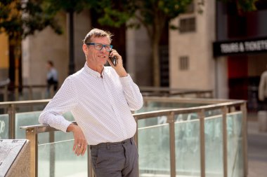 Mobil telefonda konuşurken ve kentsel alanda açık bağlı kalmak ve girişimci yaratıcı iş kavramı sokakta yürürken gülümseyen yakışıklı olgun yaratıcı serbest işadamı.