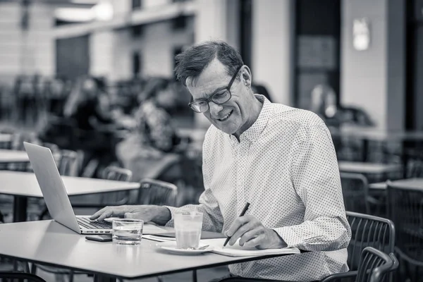 Cheerful smiling old man working on computer while having coffee in terrace coffee shop city outdoors in seniors using modern technology Staying connected and entrepreneur creative business concept.