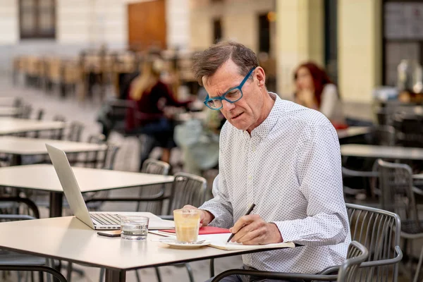 Cheerful smiling old man working on computer while having coffee in terrace coffee shop city outdoors in seniors using modern technology Staying connected and entrepreneur creative business concept.