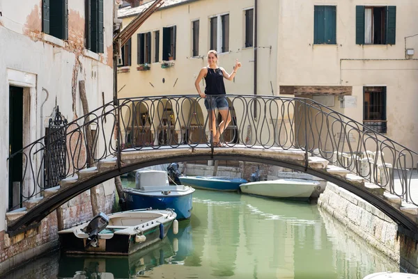 魅力的な女性の自然なラテン観光とヨーロッパ コンセプトに夏の休日旅行のヴェネツィアの運河で示す親指を笑みを浮かべてカメラを見てポーズ — ストック写真