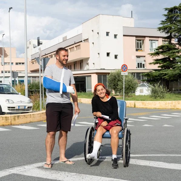 Young injured couple with broken foot and arm coming out of the hospital happy that their insurance paid the medical bills in travel health insurance concept.