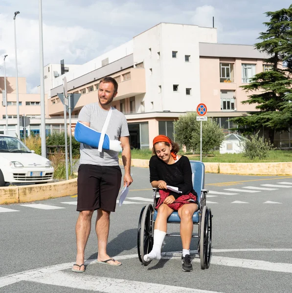 Young injured couple with broken foot and arm coming out of the hospital happy that their insurance paid the medical bills in travel health insurance concept.