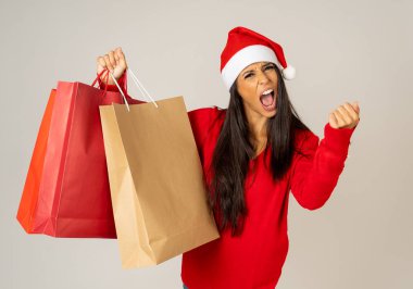 Genç kadın Noel için hazır kağıt poşetler içinde kırmızı ve Santa claus şapka ile Noel alışveriş hediye kutlama tüketicilik ve satış konsepti için hazır olmak gri arka plan izole.