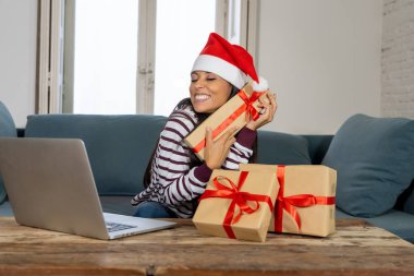 Seçme ve Noel hediyeleri oturma odasında evde bir kanepede oturan bir dizüstü bilgisayar kullanarak satırındaki alış kırmızı kazak ve santa claus şapka giyen kadın Noel için tüm hazır olması hakkında heyecanlı