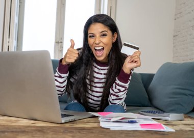 Kredi kartı hesap makinesi ve ev arıyorum, fatura ödeme dizüstü kullanan neşeli çekici latin kadın dinlenmek ev maliyesi online bankacılık online satın alma ve internet alışveriş fatura ödeme.