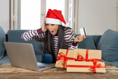 Kırmızı kazak ve kredi kartı seçme ve dizüstü evde kullanma Noel hediyeleri satın holding santa claus şapka giyen kadın Internet satış ve kredi kartı ile alışveriş çizgi üzerinde tesislerinde heyecanlı
