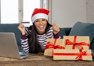 Kırmızı kazak ve kredi kartı seçme ve dizüstü evde kullanma Noel hediyeleri satın holding santa claus şapka giyen kadın Internet satış ve kredi kartı ile alışveriş çizgi üzerinde tesislerinde heyecanlı