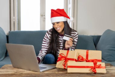 Kırmızı kazak ve kredi kartı seçme ve dizüstü evde kullanma Noel hediyeleri satın holding santa claus şapka giyen kadın heyecan Internet satış ve kredi kartı ile online alışveriş imkanları