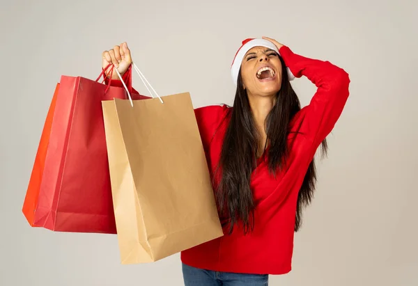 若い女性紙のショッピング バッグ赤とサンタ クロースの帽子とクリスマスの準備ができて分離クリスマス ショッピング ギフトお祝い消費と販売コンセプトのため準備ができているの灰色の背景 — ストック写真