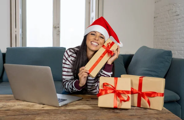 妇女穿着红色的毛衣和圣诞老人的帽子选择和购买圣诞礼物在线使用笔记本电脑坐在客厅里的沙发上兴奋着所有准备圣诞节 — 图库照片