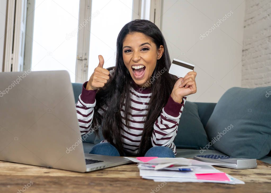 Cheerful attractive latin woman using credit card calculator and laptop paying bills at home looking relax in home finances paying bills online banking buying online and internet shopping.