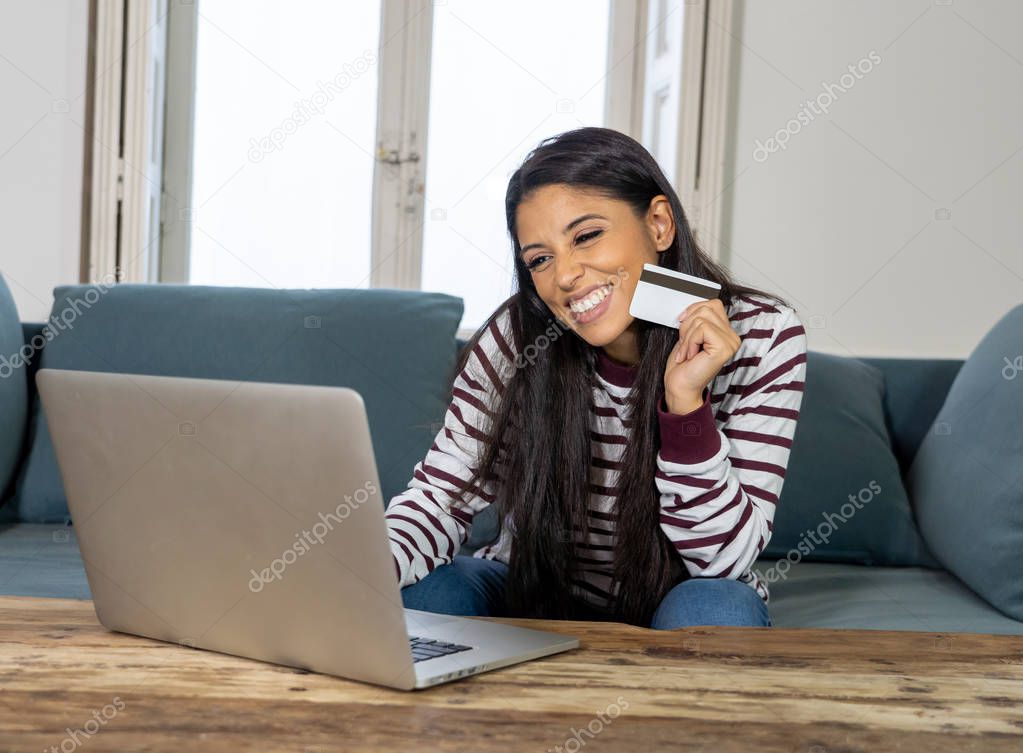 Attractive young latin woman holding credit card and using laptop computer buying on the internet at home in shopping on line business and technology digital marketing casual lifestyle concept.