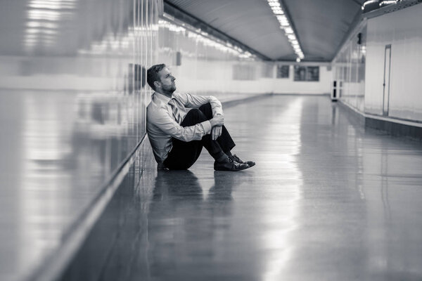 Young jobless business man suffering depression sitting on ground street underground leaning on wall alone looking desperate in Emotional pain Mental health Unemployment and Human emotions concept.