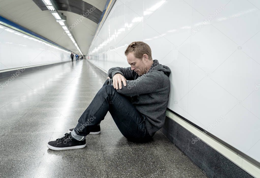 Miserable jobless young man crying Drug addict Homeless in depression stress sitting on ground street subway tunnel looking desperate leaning on wall alone in Mental disorder Emotional pain Sadness.