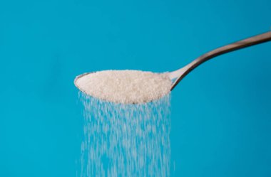 Pour bir kaşık bir akıştaki olmak şeker ın Too mavi arka plan üzerinde izole kadar şeker tatlı bağımlılığı diyabet hastalığı sağlıksız yiyecek kavramı.