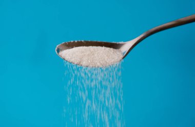 Pour bir kaşık bir akıştaki olmak şeker ın Too mavi arka plan üzerinde izole kadar şeker tatlı bağımlılığı diyabet hastalığı sağlıksız yiyecek kavramı.