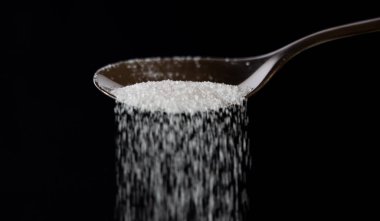 Pour bir kaşık bir akıştaki olmak şeker siyah koyu arka planda çok fazla şeker tatlı bağımlılığı diyabet hastalığı sağlıksız gıda kavramı izole.