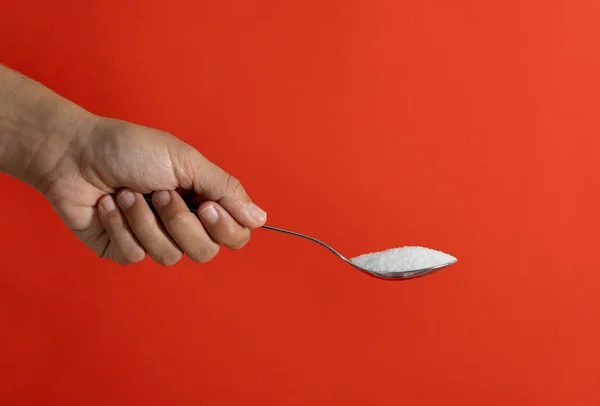 Close up of woman hand offering coffee spoon full of sugar isolated on red background in of sugar addiction too much calories and unhealthy food concept