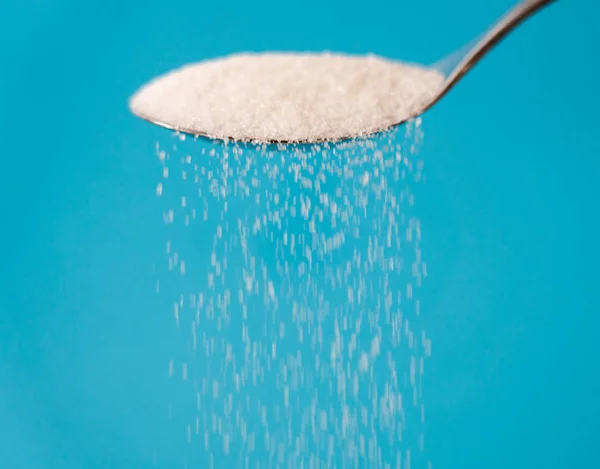 Sugar being pour from a spoon in a stream isolated on blue background in Too much sugar Sweet addiction diabetes disease unhealthy food concept.