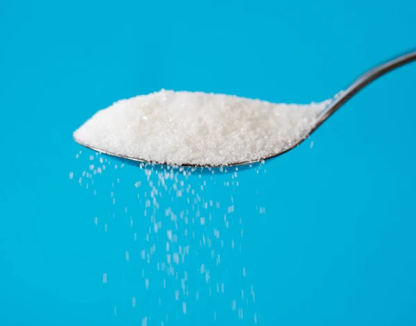 Sugar being pour from a spoon in a stream isolated on blue background in Too much sugar Sweet addiction diabetes disease unhealthy food concept.