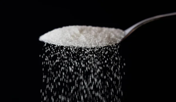 糖被从勺子倒在黑色深色背景的流中 糖甜成瘾糖尿病疾病不健康食品概念 — 图库照片