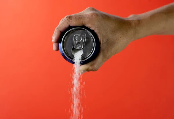 Hand holding soda can pouring crazy amount of sugar in metaphor of sugar content of refreshing drink isolated on red background in Nutrition Diet Unhealthy food Addiction and Excess calories content.