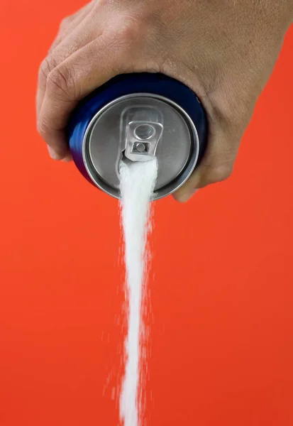 Hand holding soda can pouring crazy amount of sugar in metaphor of sugar content of refreshing drink isolated on red background in Nutrition Diet Unhealthy food Addiction and Excess calories content.