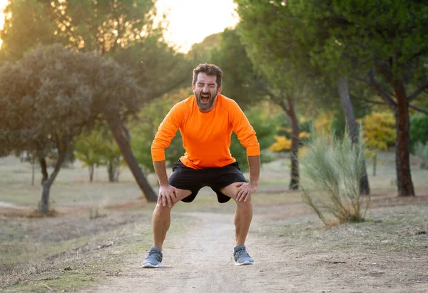 Young fit man holding knee with his hands in pain after suffering muscle injury broken bone leg pain sprain or cramp during a running workout in park outdoors in sport training running injury.