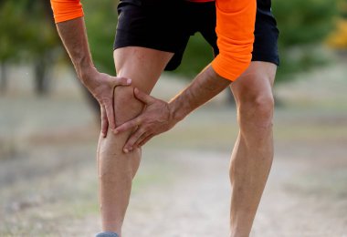 Young fit man holding knee with his hands in pain after suffering muscle injury broken bone leg pain sprain or cramp during a running workout in park outdoors in sport training running injury. clipart