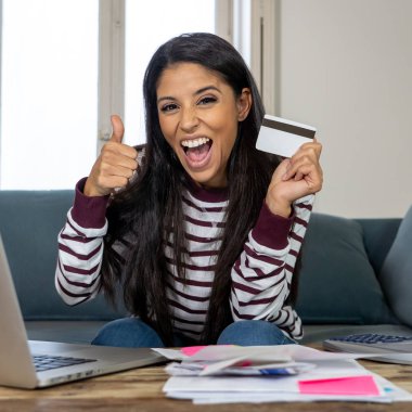 Kredi kartı hesap makinesi ve ev arıyorum, fatura ödeme dizüstü kullanan neşeli çekici latin kadın dinlenmek ev maliyesi online bankacılık online satın alma ve internet alışveriş fatura ödeme.