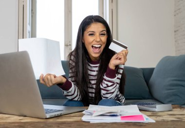 Kredi kartı hesap makinesi ve ev arıyorum, fatura ödeme dizüstü kullanan neşeli çekici latin kadın dinlenmek ev maliyesi online bankacılık online satın alma ve internet alışveriş fatura ödeme.