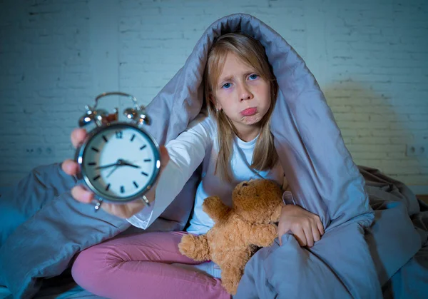 Симпатична Безсонна Дівчинка Сидить Ліжку Показуючи Будильник Який Виглядає Втомленим — стокове фото