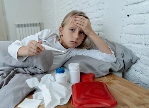 可爱的生病的女孩在疼痛与高烧和头痛感觉不适躺在床上与药物温度计热水袋冷和冬季流感病毒和条纹症状在儿童保健概念 — 图库照片