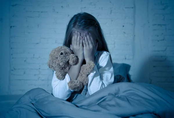 Przestraszona Dziewczynka Siedzi Łóżku Zasłaniając Twarz Rękami Trzymając Jej Teddy — Zdjęcie stockowe