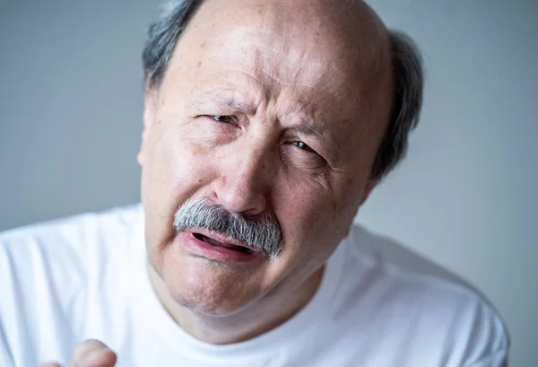 Portrait of older adult senior man in pain with sad and exhausted face in human emotions facial expression retirement and depression concept isolated on neutral background.