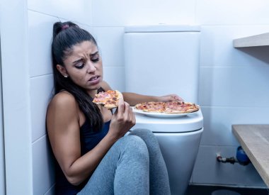 Duygu suçlu ve hasta yerde yeme bozuklukları anoreksiya ve bulimia kavramı tuvalete yanında otururken yemek çekici genç ve üzgün bulimik genç kadın.