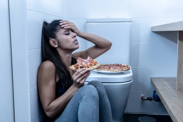 魅力的な若いと悲しい過食症若い女性有罪と摂食障害の拒食症と過食症の概念のトイレの横の床に座って食事が病気を感じ — ストック写真
