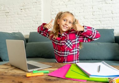 Sevimli beyaz neşeli İlköğretim öğrenci ödev yapmak ve onun laptop yeni teknoloji okul eğitim kavramı içinde oturma odasında evde eğitim sırasında mutlu hissediyor.