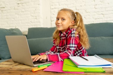 Sevimli beyaz neşeli İlköğretim öğrenci ödev yapmak ve onun laptop yeni teknoloji okul eğitim kavramı içinde oturma odasında evde eğitim sırasında mutlu hissediyor.