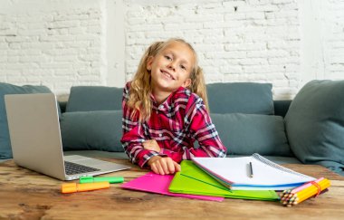 Sevimli beyaz neşeli İlköğretim öğrenci ödev yapmak ve onun laptop yeni teknoloji okul eğitim kavramı içinde oturma odasında evde eğitim sırasında mutlu hissediyor.