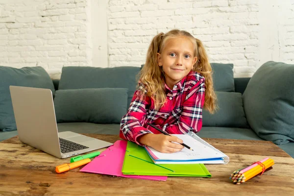 Sevimli beyaz neşeli İlköğretim öğrenci ödev yapmak ve onun laptop yeni teknoloji okul eğitim kavramı içinde oturma odasında evde eğitim sırasında mutlu hissediyor.
