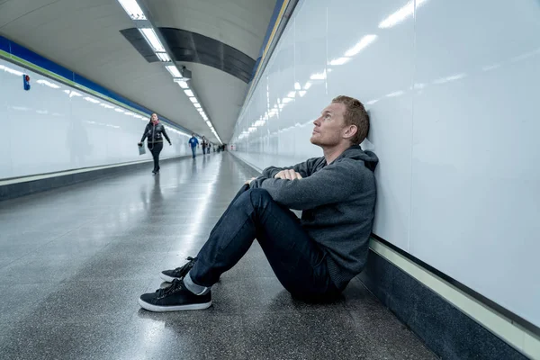 Miserable jobless young man crying Drug addict Homeless in depression stress sitting on ground street subway tunnel looking desperate leaning on wall alone in Mental disorder Emotional pain Sadness.