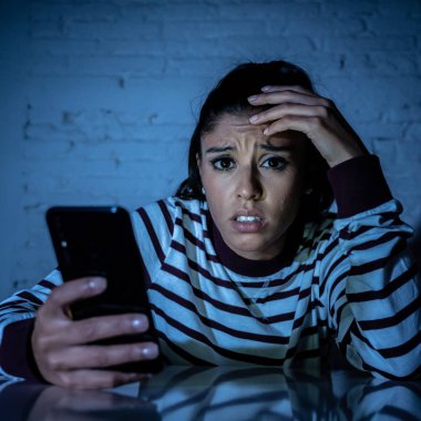 Frightened teenager or young woman using smart mobile cell phone as internet cyberbullying by message stalked abused victim. clipart