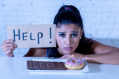 Young worried latin woman feeling tempted and guilty wanting to eat chocolate and donuts asking for help in diet calories sugar addiction nutrition and lifestyle concept. clipart