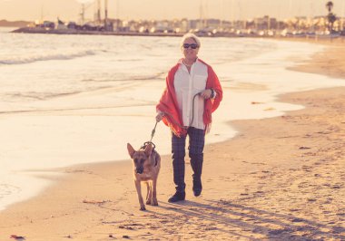 Güzel emekli yaşlı kadın ve plaj arkadaşlık faydaları hayvanların koruma aktif emeklilik yaşam tarzı ve köpek dostu Turizm kıyı deniz okyanus yürürken Alman shepard köpeği.