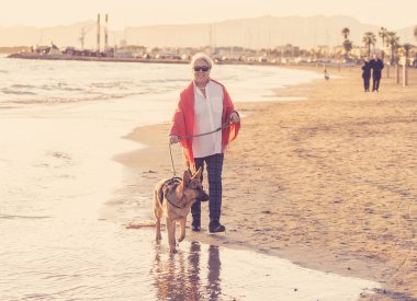 Güzel emekli yaşlı kadın ve plaj arkadaşlık faydaları hayvanların koruma aktif emeklilik yaşam tarzı ve köpek dostu Turizm kıyı deniz okyanus yürürken Alman shepard köpeği.
