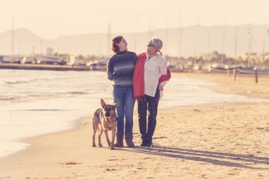 Mutlu kıdemli anne yetişkin kızı ve Alman shepard köpek vakit birlikte günbatımı ışık kumsalda mutlu aile anlarda evde beslenen hayvan hayvanlar yürürken köpek dostu Turizm ve emeklilik faydaları.
