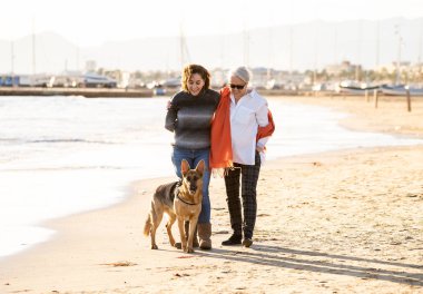 Mutlu kıdemli anne yetişkin kızı ve Alman shepard köpek vakit birlikte günbatımı ışık kumsalda mutlu aile anlarda evde beslenen hayvan hayvanlar yürürken köpek dostu Turizm ve emeklilik faydaları.