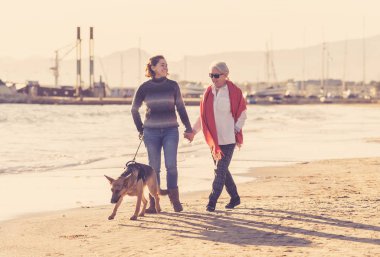 Mutlu kıdemli anne yetişkin kızı ve Alman shepard köpek vakit birlikte günbatımı ışık kumsalda mutlu aile anlarda evde beslenen hayvan hayvanlar yürürken köpek dostu Turizm ve emeklilik faydaları.