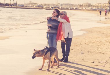 Mutlu kıdemli anne yetişkin kızı ve Alman shepard köpek vakit birlikte günbatımı ışık kumsalda mutlu aile anlarda evde beslenen hayvan hayvanlar yürürken köpek dostu Turizm ve emeklilik faydaları.